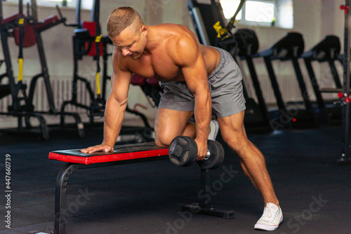 Strongman bodybuilder exercising with dumbbell in a modern gym.Copy space.