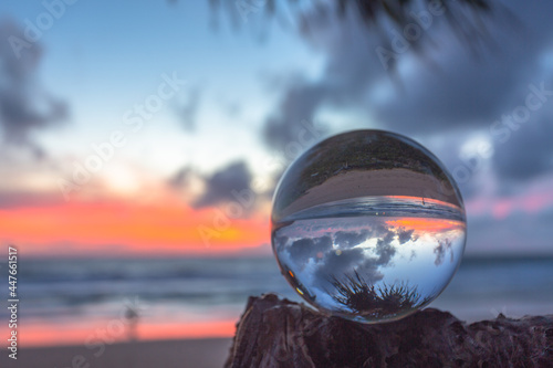 beautiful cloud moving and red sunset inside crystal ball placed on a branch beside the beach. Unique and creative travel and nature idea. © Narong Niemhom