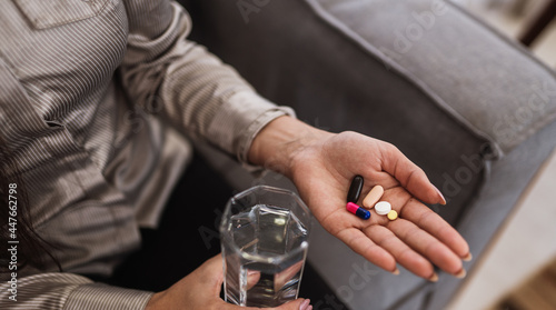 Close up of woman holding various tablets, pills and glass of water. Taking vitamins, medications, and dietary supplements. The concept of disease prevention and treatment, healthcare concept.