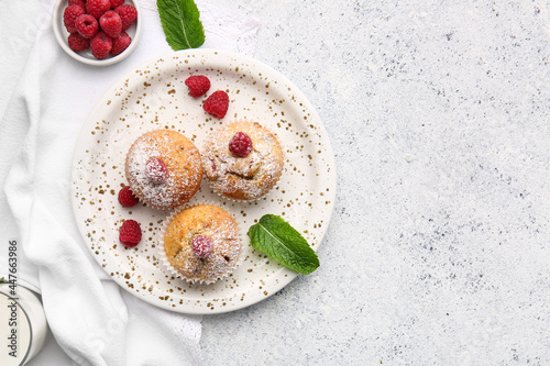Plate with tasty raspberry muffins on light background