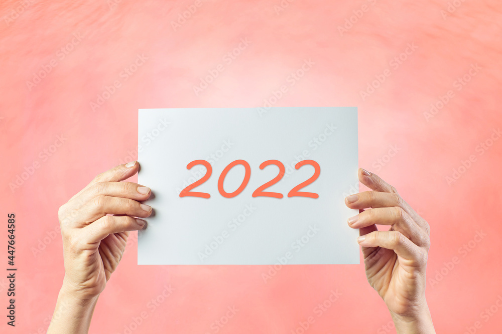 Woman holding with both hands a cardboard with the number 2022 on a pink background. New year concept
