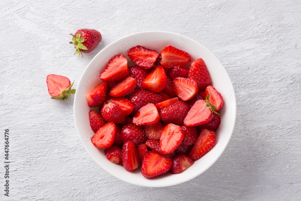 White bowl with fresh chopped strawberries on a light gray background White bowl with fresh chopped strawberries on a light gray background
