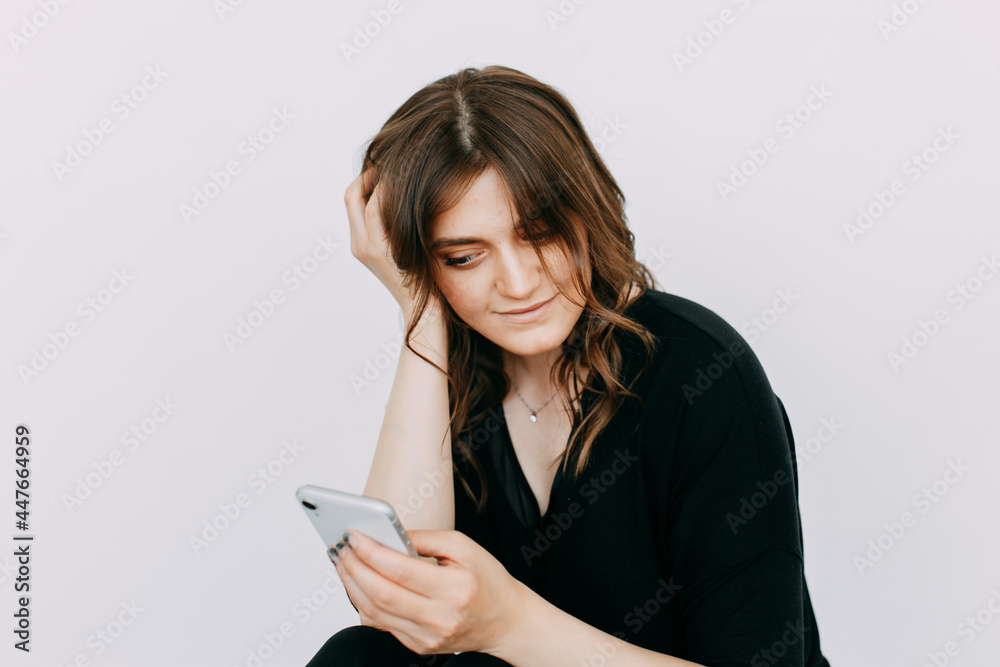 A freelance businesswoman is a young woman in casual clothes talking on the phone working using wireless technologies sitting on the floor against a white wall in an empty room at home A freelance businesswoman is a young woman in casual clothes talking on the phone working using wireless technologies sitting on the floor against a white wall in an empty room at home