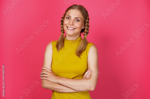 Waist-high portrait of young cheerful smiling woman with pigtails standing isolated over pink background