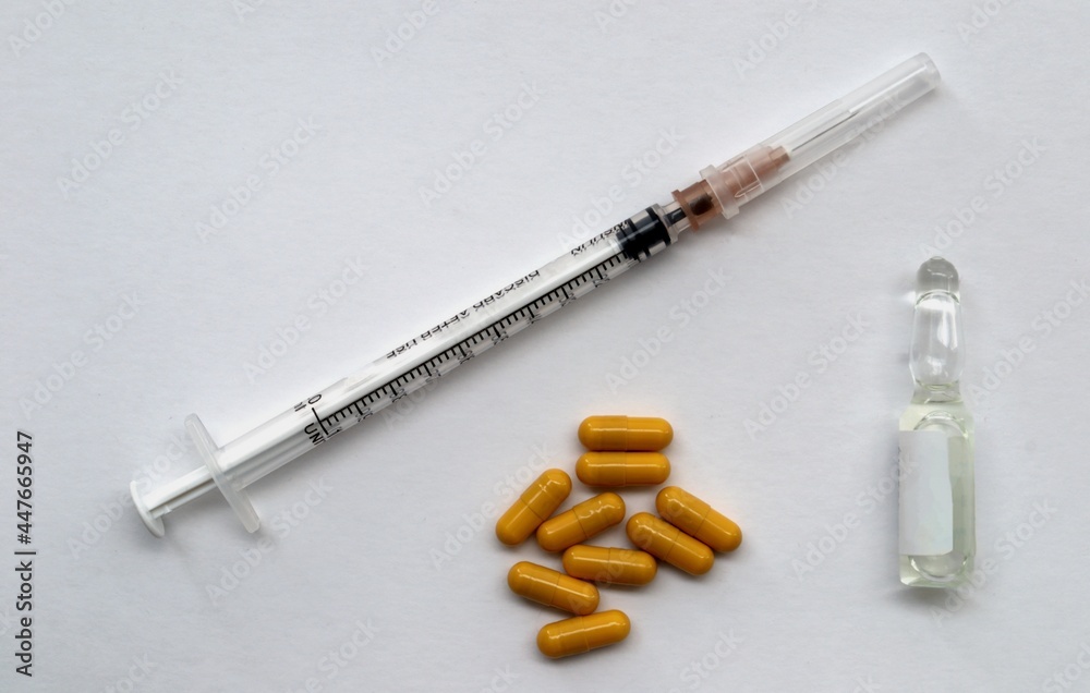 A syringe, yellow tablets and an ampoule for injection on a white background A syringe, yellow tablets and an ampoule for injection on a white background