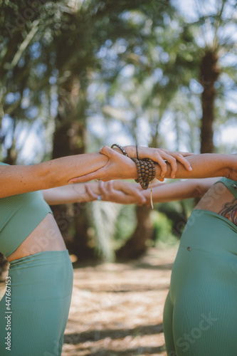 Detail of the hands of two girls doing yoga in nature.