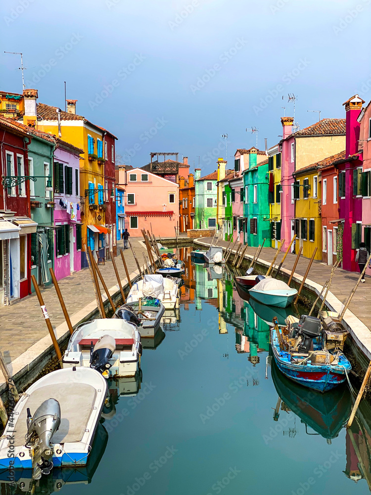 Boats docking and colorful houses in a canal street houses on Burano island, Venice, One unrecognizable people on the background.