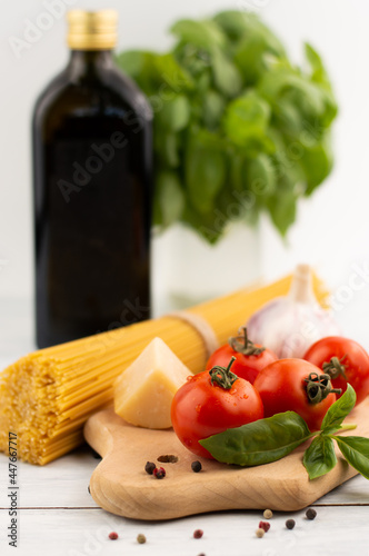Blurred image of tomato, basil, garlic, parmesan, spaghetti on a cutting board, olive oil and a bunch of basil in the background.Proper nutrition.