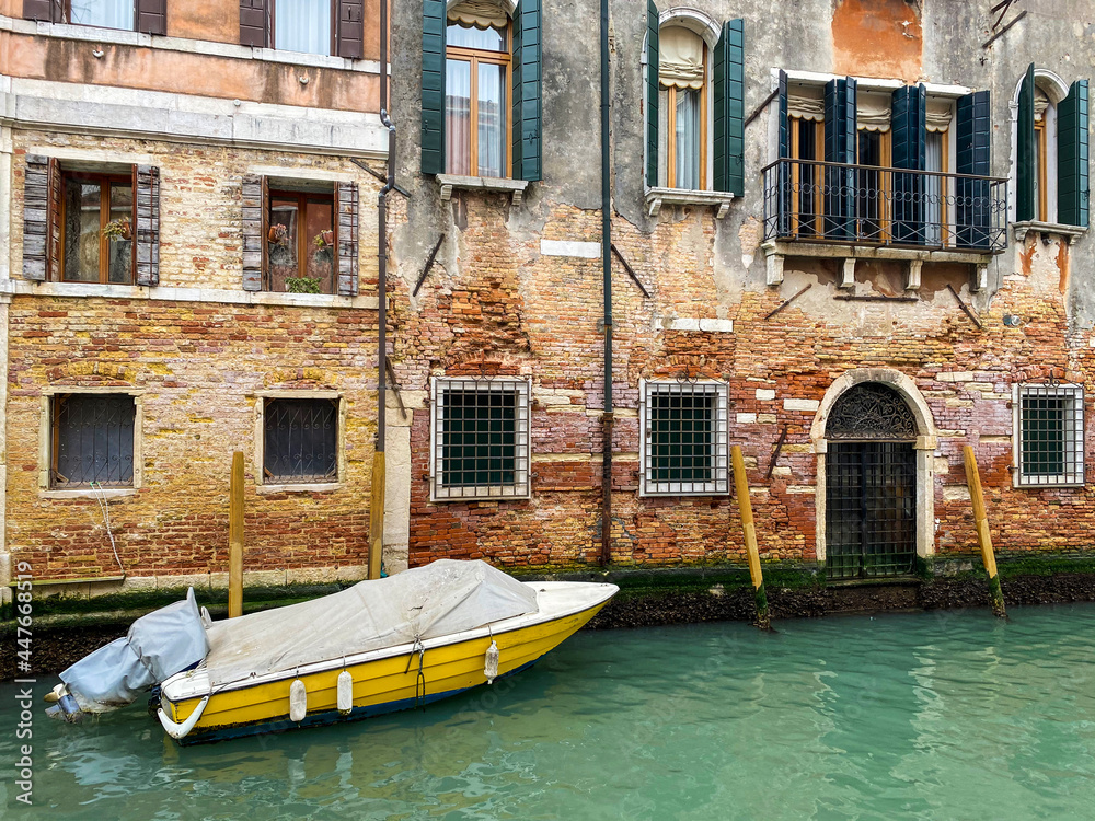 Side view of a yellow boat docking in front of a old red bricks venetian house Side view of a yellow boat docking in front of a old red bricks venetian house