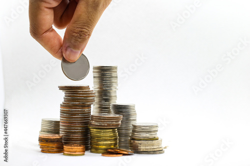 Investment concept and finance theme. Hand holding coins drop down to piles of gold and metal coins on white background.