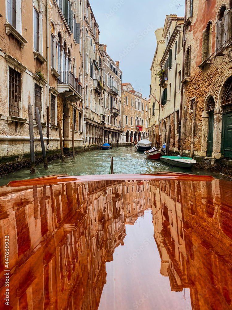 Houses reflections on the Varnished wooden hood, pontoon, of the water taxi in the streets of Venice, which leaves