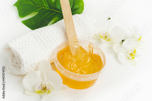 Sugar paste or wax honey in a transparent jar and white orchid on a white background. Sugaring. Depilation and beauty concept. Waxing. Close up shot.
