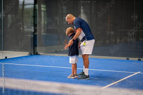 Monitor teaching padel class to child, his student - Trainer teaches little boy how to play padel on indoor tennis court