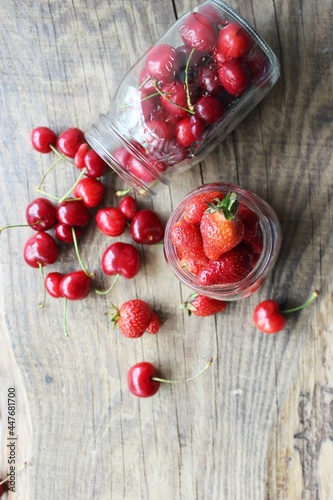 Ripe strawberries and cherries , glass jars. Wood background, rustic style. The concept of making jam, homemade preparations