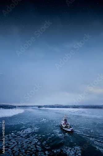 Tug boat in calm icy water in winter and stars in the sky. Peaceful artistic image.