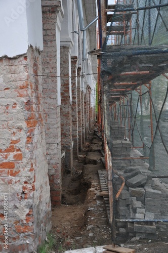 Passage into the distance. Old walls of the building and restoration scaffolding. Green grid. Piles of bricks. 