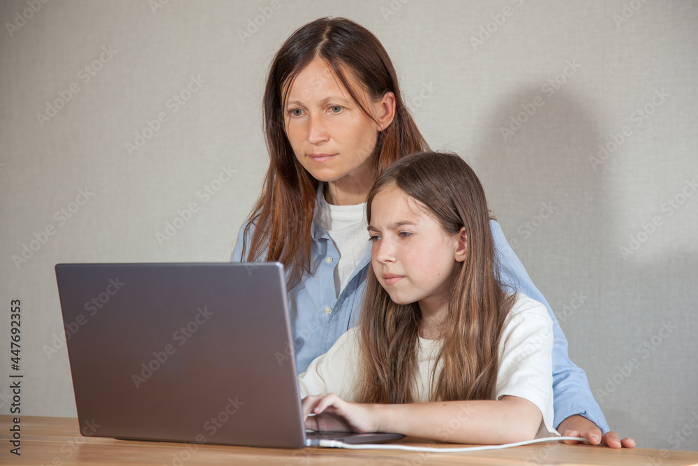 a mother and a teenage girl are sitting at a table and looking at a laptop. The concept of homework, distance learning a mother and a teenage girl are sitting at a table and looking at a laptop. The concept of homework, distance learning