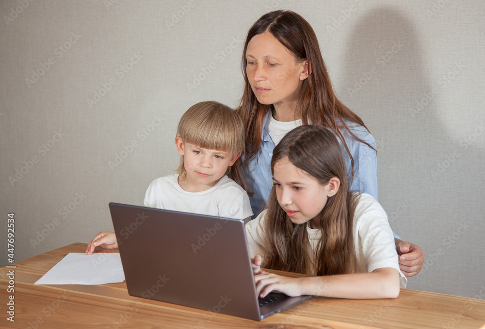 a teenage girl works on a laptop, her mother helps her , and her younger brother watches and studies. The concept of distance learning or homework
