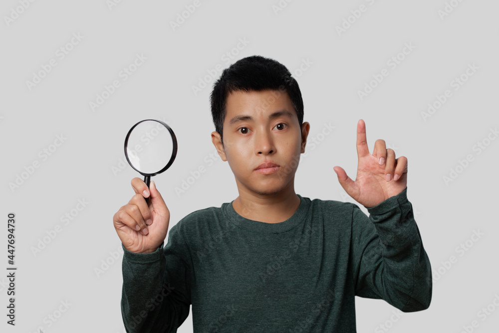 Young man holding magnifying glass and point index finger up with new idea on gray background. Young man holding magnifying glass and point index finger up with new idea on gray background.