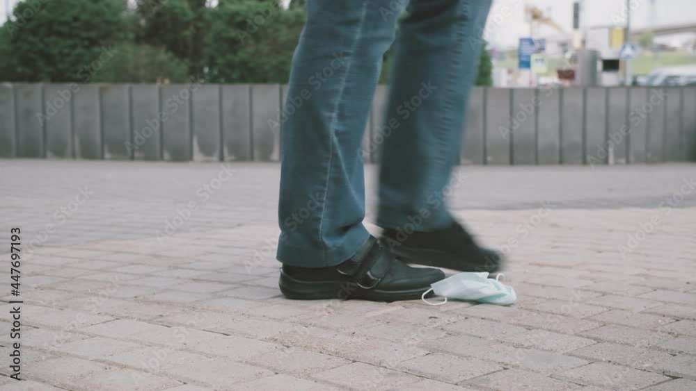 Person walks down a city street and throws a medical mask against the virus on the ground. The concept of fatigue from the limitations of the epidemic and pandemic and the removal of lockdown Person walks down a city street and throws a medical mask against the virus on the ground. The concept of fatigue from the limitations of the epidemic and pandemic and the removal of lockdown