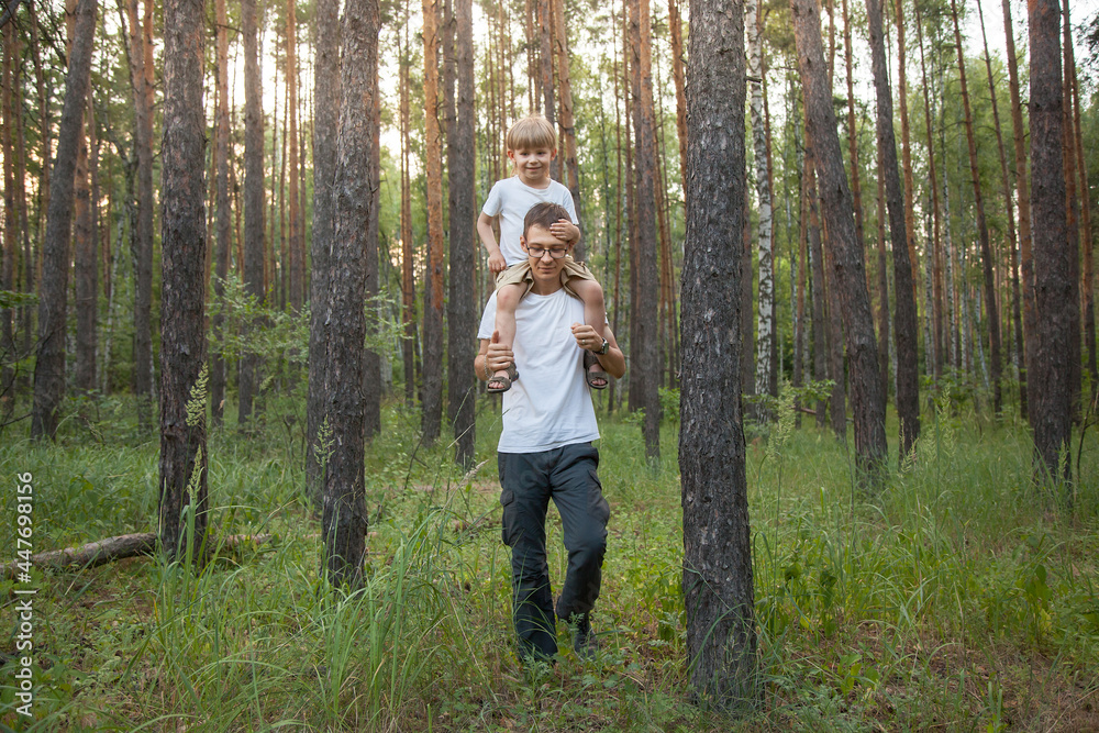 dad and son are walking through the forest. The father carries the boy on his shoulders, they are happy