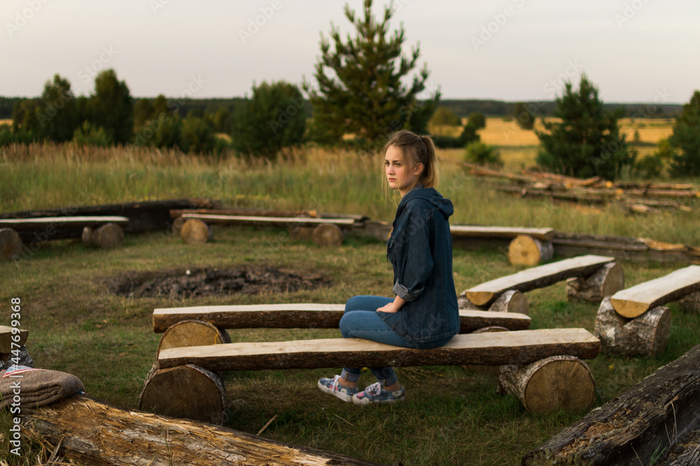 Young girl sitting on logs near costar site camp summer sunset countryside Young girl sitting on logs near costar site camp summer sunset countryside