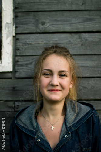 Portrait of a young smilingfair-haired white girl of European appearance at sunset on the background of a wooden wall of gray boards photo