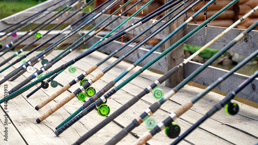 Many fishing rods on the wooden pier by the river or lake on a sunny day