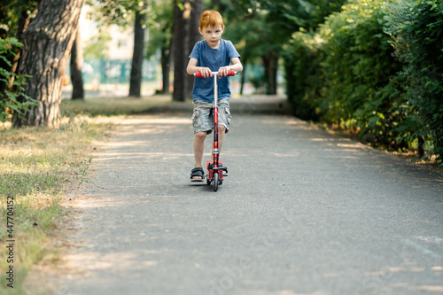 Young boy rides a scooter on the road in summer. © Konstiantyn Zapylaie