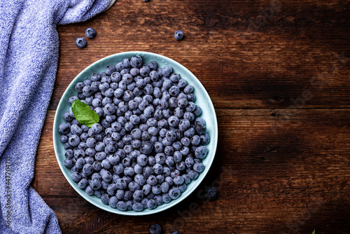 Fresh blueberries berries in a plate on a dark wooden background.