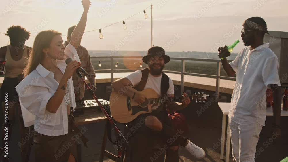 Slowmo of musicians performing song at party on rooftop terrace on nice summer evening