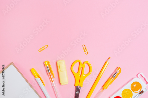 Back to school. Composition with opened copybook and yellow office supplies on pink background. Flat lay. Copy space. Concept of education and creativity