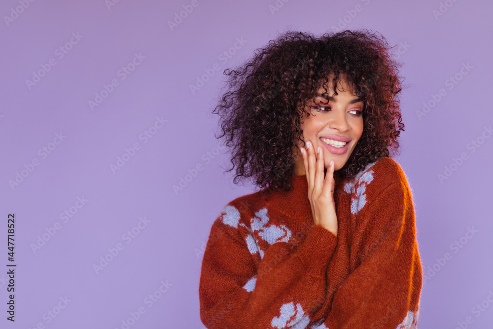 Close-up studio portrait of brunette curly woman smiling on purple background. Dark-skinned happy lady in red sweater poses on isolated. Close-up studio portrait of brunette curly woman smiling on purple background. Dark-skinned happy lady in red sweater poses on isolated.