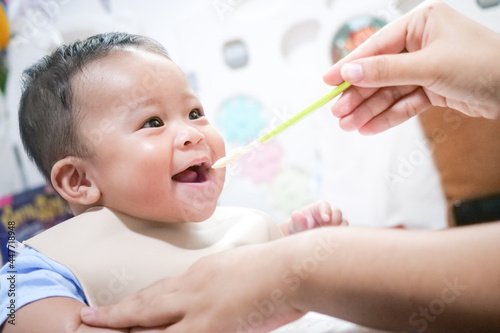 A happy asian baby boy sitting and feeding some pap pudding by mom with spoon.