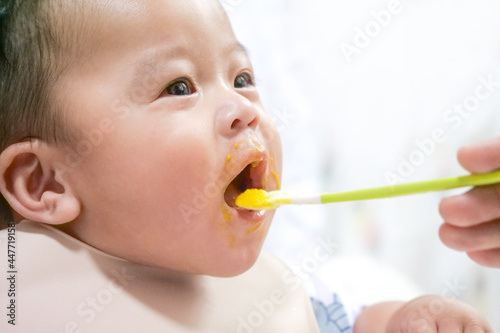 A happy asian baby boy sitting and feeding some pap pudding by mom with spoon.