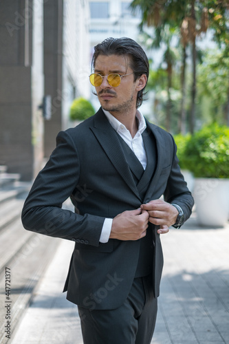 Portrait of handsome young man in black formal suit and yellow sunglasses looking aside
