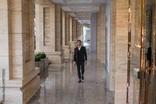 Office worker in black suit walking on the street near modern office building.  © Aleksandr