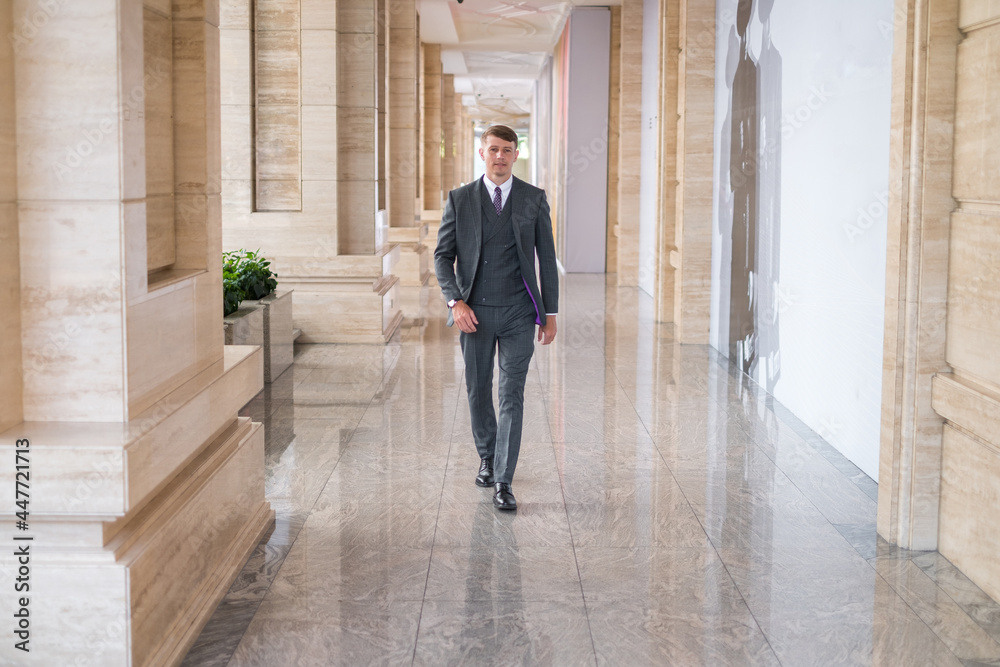Businessman wearing grey suit and walking near office buiding
