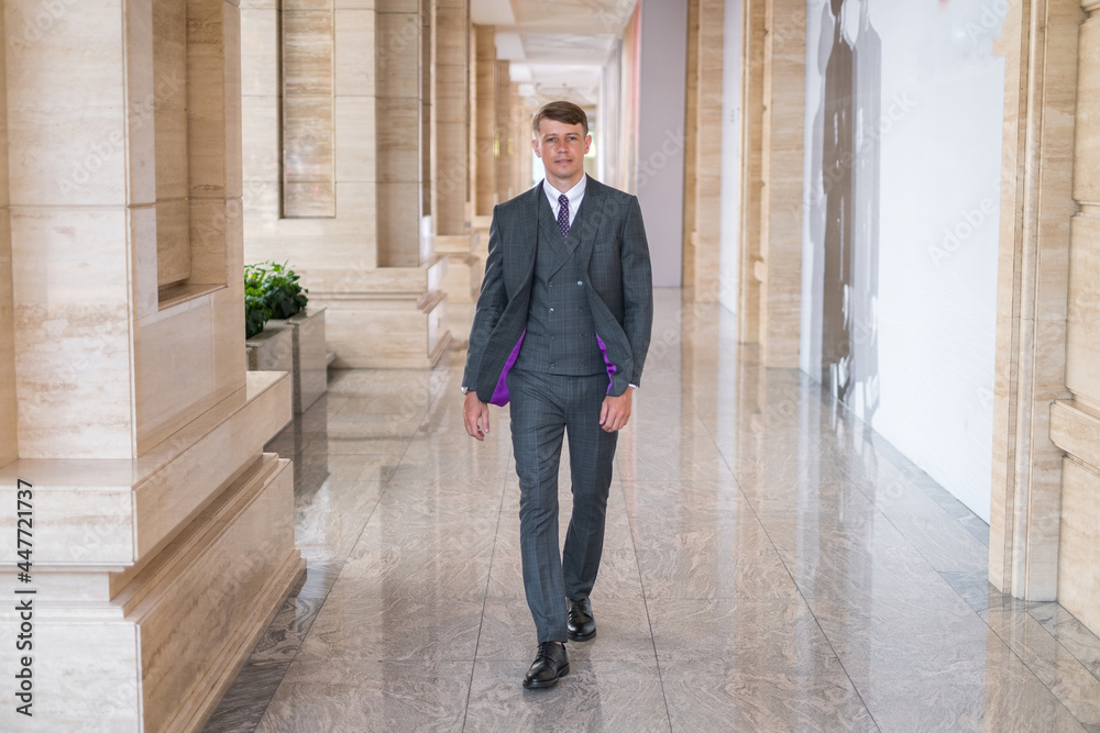 Businessman wearing grey suit and walking near office buiding

