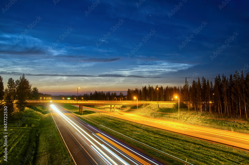 Fototapeta premium Motion blur of busy highway going through rural landscape with nice clouds at night and car light trails with long exposure. Background 
