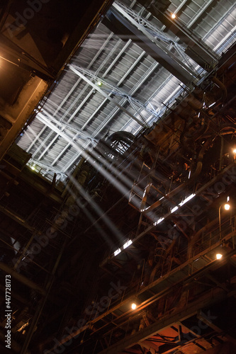 Interior of electric power plant with giant boiler (right). Sun rays in steamed air. Profile roof. Aksu, Kazakhstan.