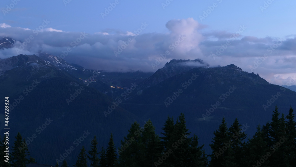 Silhouette of mountains in fog the night with fir trees in the foreground.