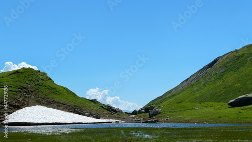 View of a lake in the mountains. Firn at the water's edge in the Alps. Pastures in the background.