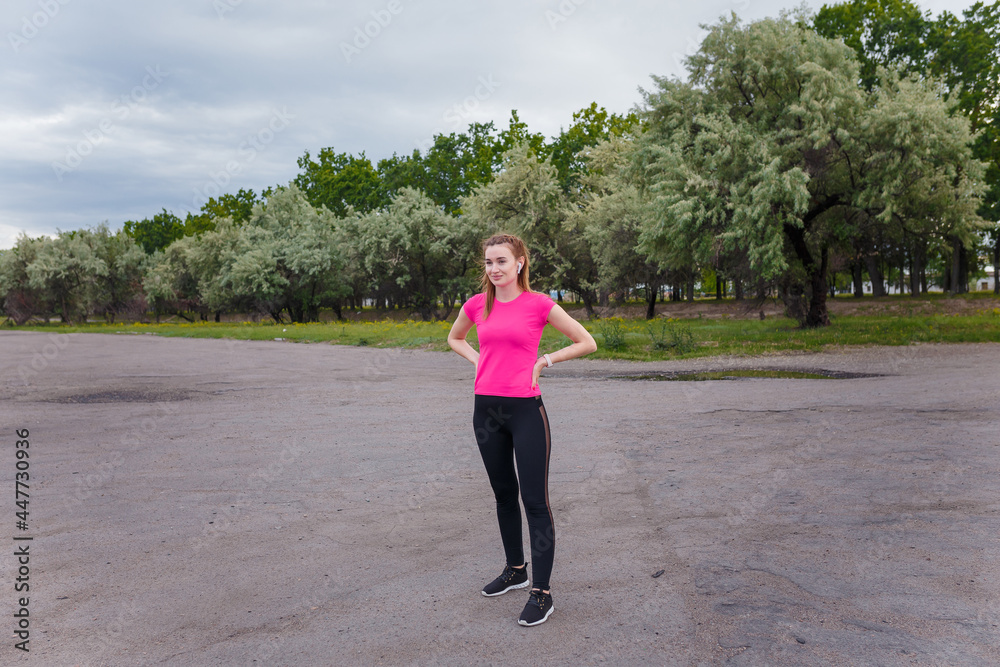 Smiling young smiling woman in sportswear and wireless earphones getting ready for outdoors running or physical training.
