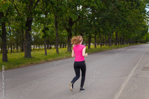 Young woman in sportswear running outdoors on green trees background. Sport, healthy way of life, runners training concept.