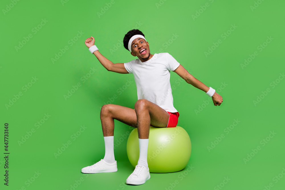 Full length photo of funny sweet dark skin guy dressed sport outfit sitting fitball warming up isolated green color background Full length photo of funny sweet dark skin guy dressed sport outfit sitting fitball warming up isolated green color background