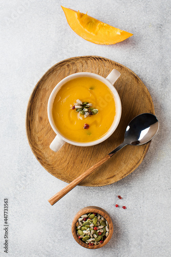 Pumpkin cream soup in a bowl with seeds on a gray background. Comfortable riding, autumn menu. 