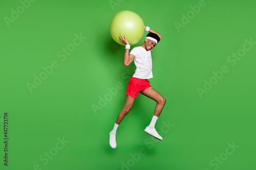 Fototapeta Naklejka Na Ścianę i Meble -  Profile photo of sportive guy jump hold big fitball wear t-shirt shorts sneakers isolated green color background