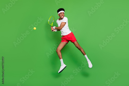 Photo of tennis player guy jump hold racquet wear white t-shirt shorts sneakers isolated green color background © deagreez