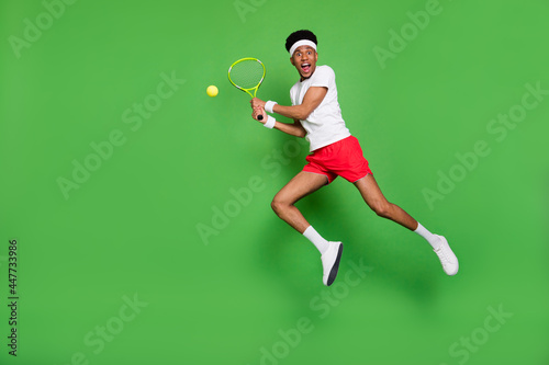 Full length photo of cute funky dark skin man wear white t-shirt jumping high playing squash isolated green color background © deagreez